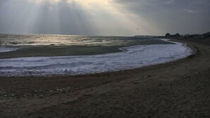 Una playa con olas, cielo despejado y un edificio a lo lejos.