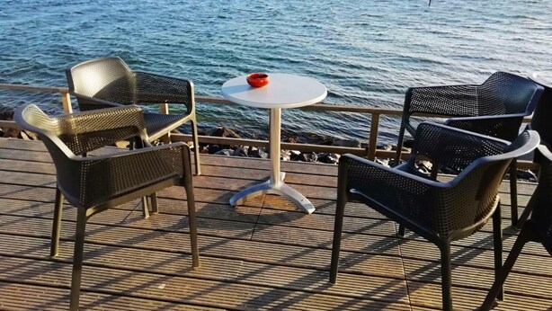 Una terraza con dos sillas de mimbre y una mesa redonda pequeña, con vistas a un mar tranquilo y una costa lejana.