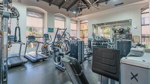 Ett gym med olika typer av träningsredskap, stora fönster och ett högt tak.