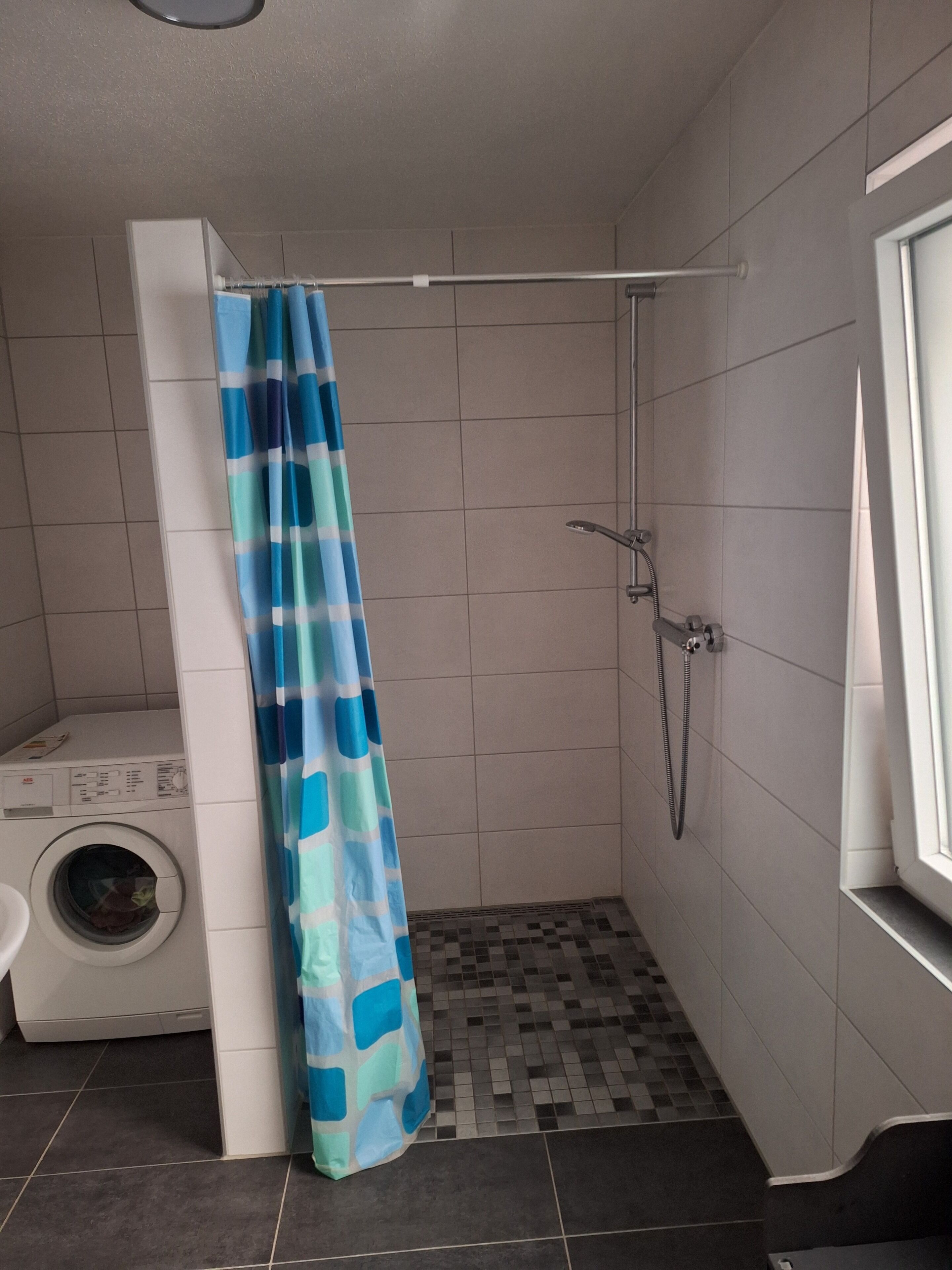 Een compacte, moderne badkamer met een douche, een wasmachine en een toilet.