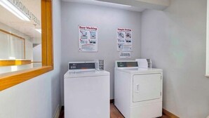 Un lavadero con dos lavadoras y secadoras, suelo de madera y carteles informativos en la pared.
