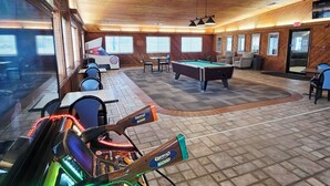 Un espacio recreativo interior con paredes de madera, una mesa de billar y máquinas de videojuegos.