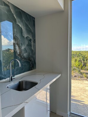 Eine moderne Küche mit Marmor-Spritzschutz, einer Edelstahl-Spüle und Blick auf einen Weinberg durch ein großes Fenster.