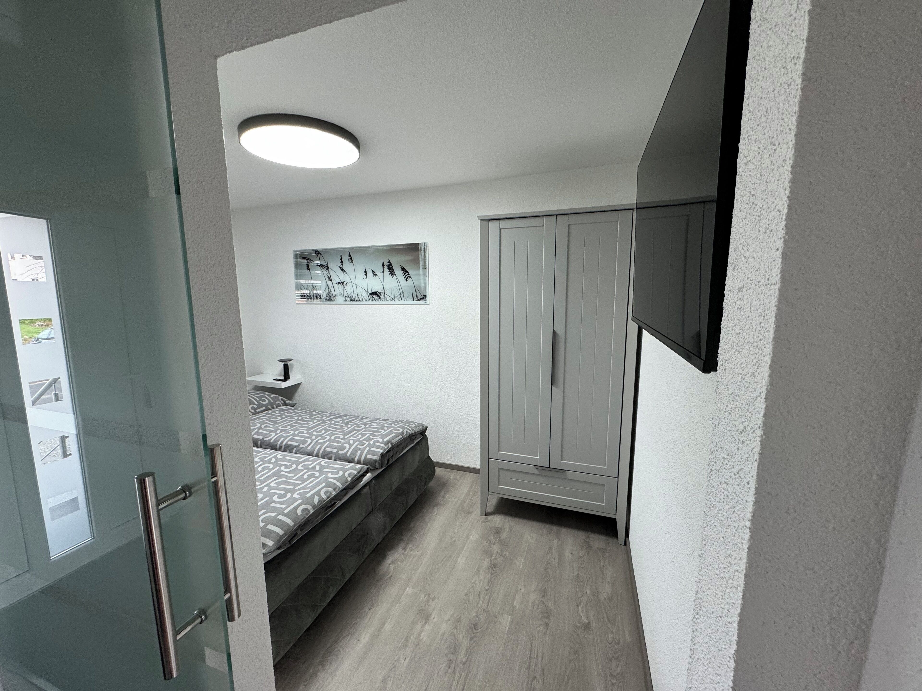 Un dormitorio con cama, armario, mesita de noche y una lámpara en el techo.