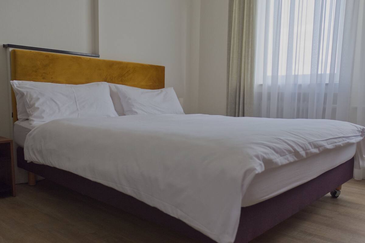 A bed with a wooden frame and a yellow headboard, white bedding, and a wooden floor.