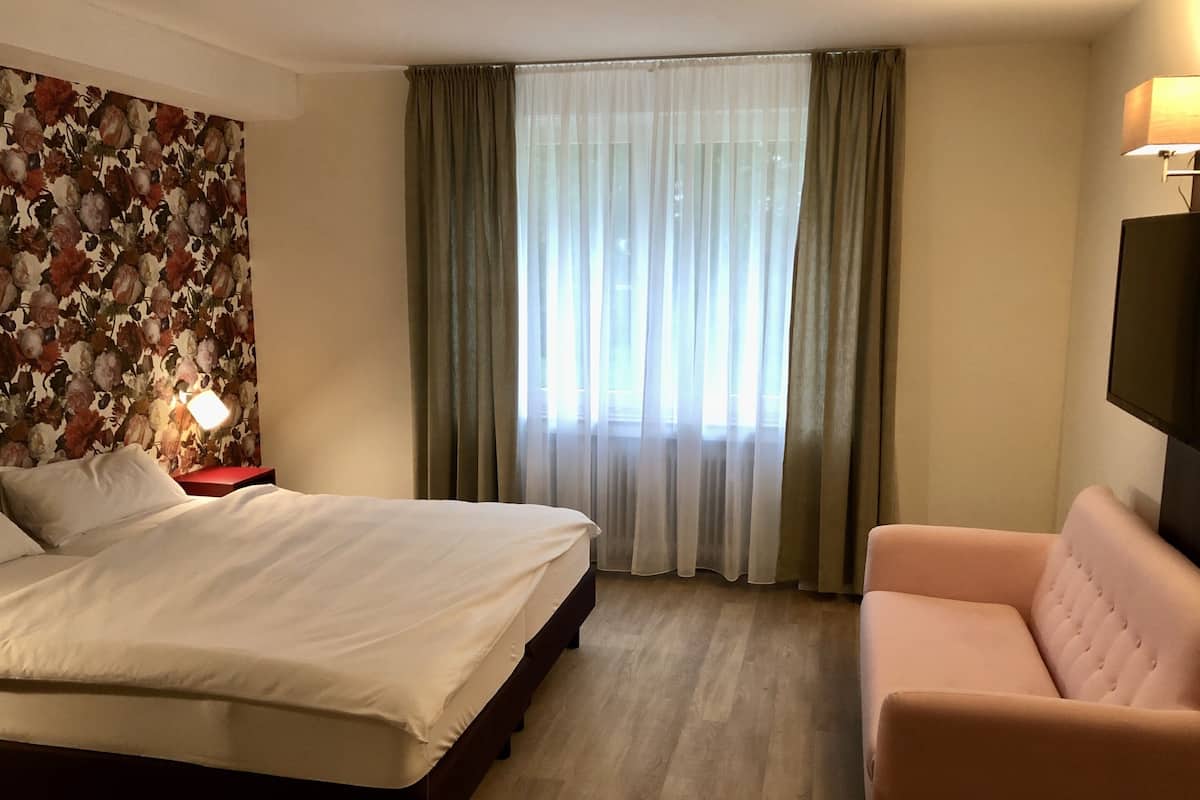 A hotel room with a bed, a chair, a nightstand, a lamp, and a TV.