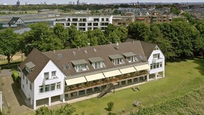 Un grand immeuble à plusieurs étages, doté d’un toit plat et de nombreuses fenêtres, entouré de verdure et d’autres bâtiments.