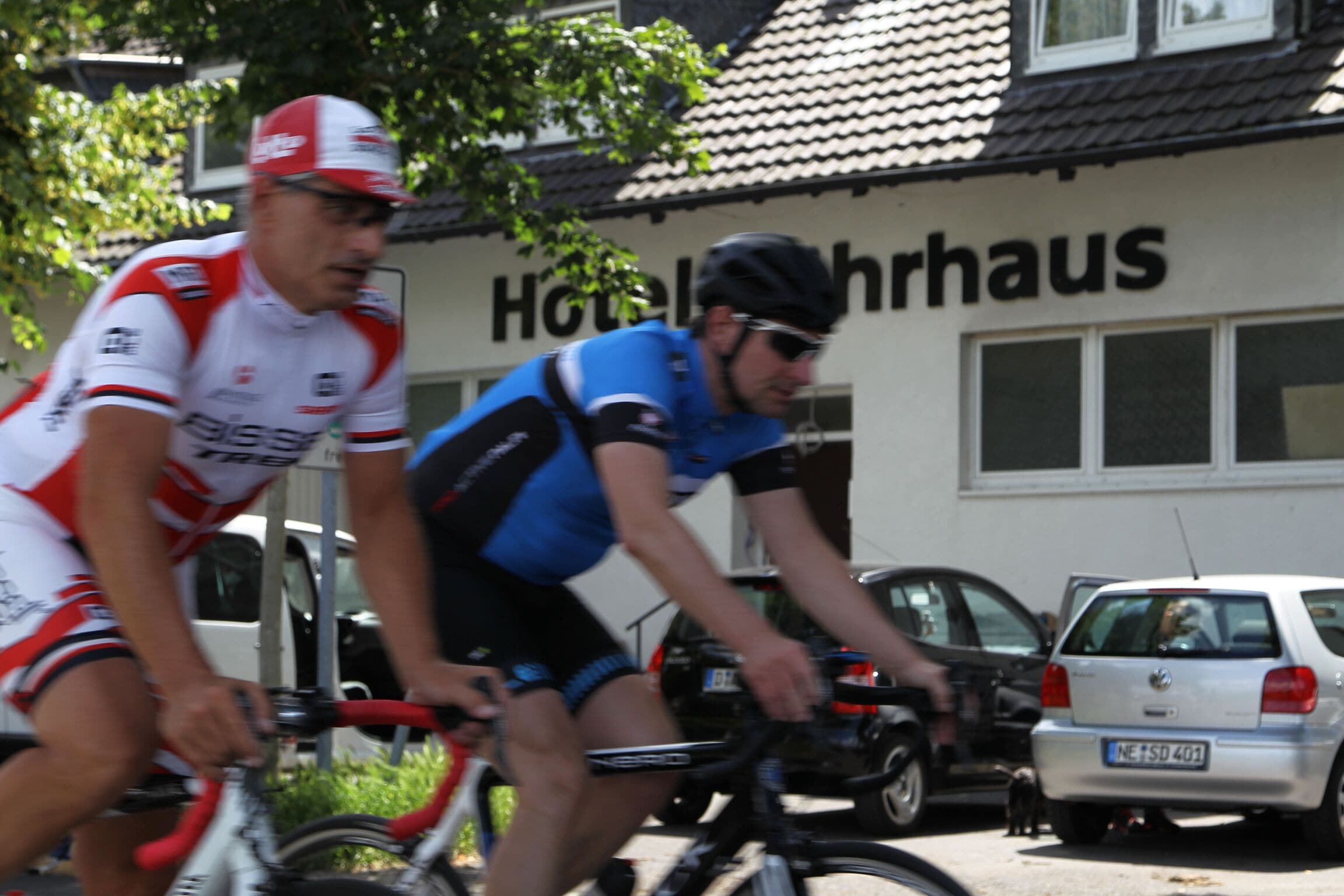 Deux cyclistes devant un bâtiment sur lequel on peut lire l’inscription « Hôtel ».