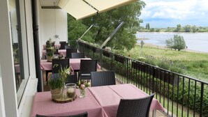 Un balcon avec des tables et des chaises, donnant sur une rivière.