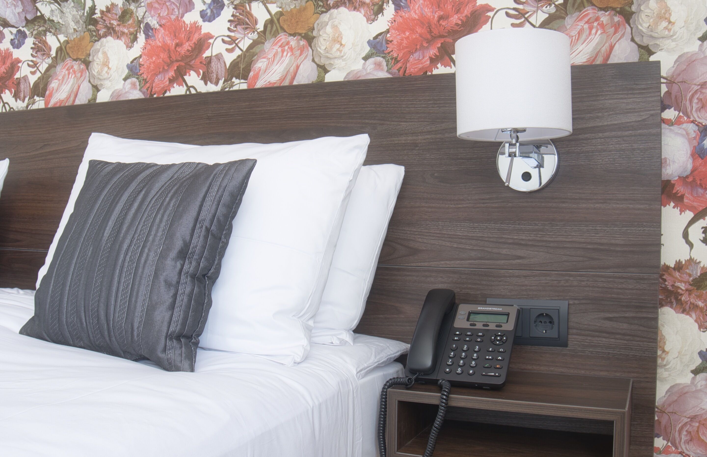 A hotel room with a bed, a bedside telephone, and a wall-mounted lamp.