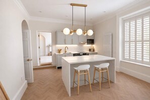 A modern kitchen with a central island, pendant lighting, and a view to the outside. - The Bridge - Apartment One (York)