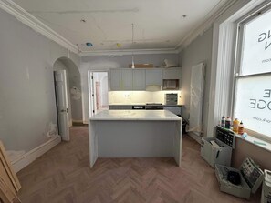 A modern kitchen with a central island, built-in cabinets, and a herringbone floor pattern. - The Bridge - Apartment One (York)