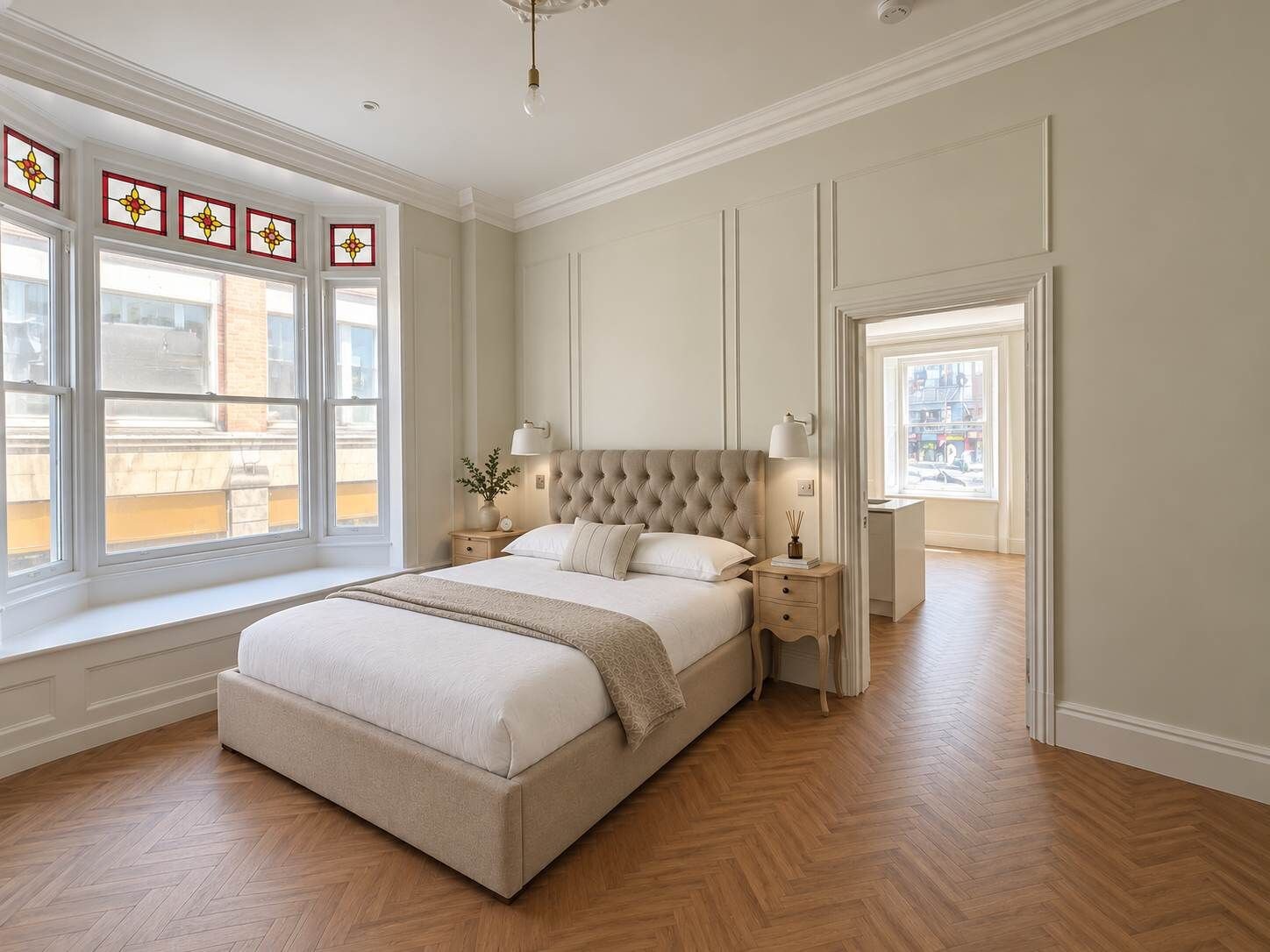 A bedroom with a large bed, a nightstand, a lamp, and a window with decorative glass panes.
