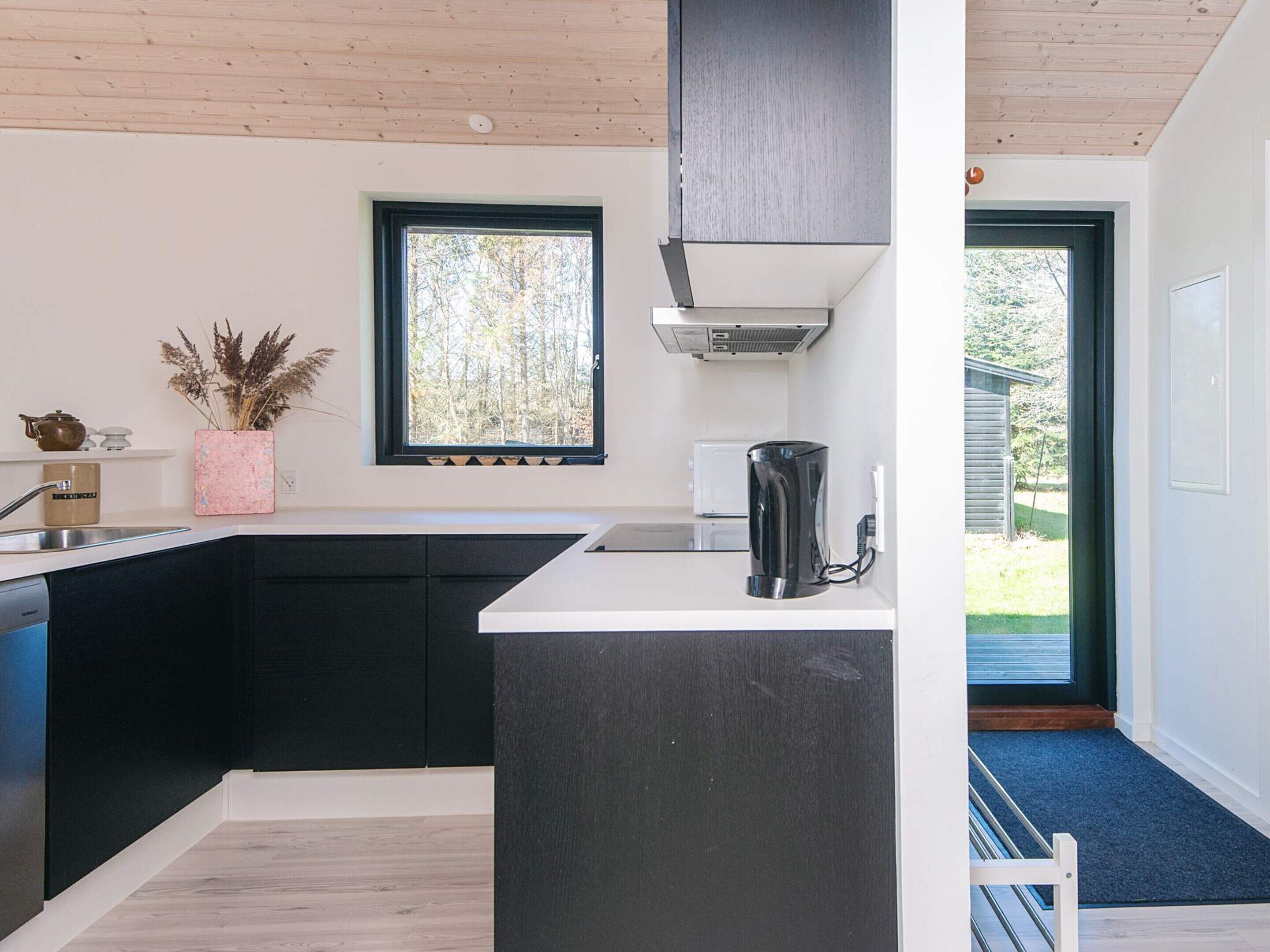 Cozinha moderna com bancada preta, cafeteira e janela com vista para árvores.
