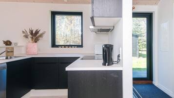 Cozinha moderna com bancada preta, cafeteira e janela com vista para árvores.