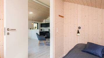 Quarto com cama, porta que dá para uma cozinha e uma cadeira.
