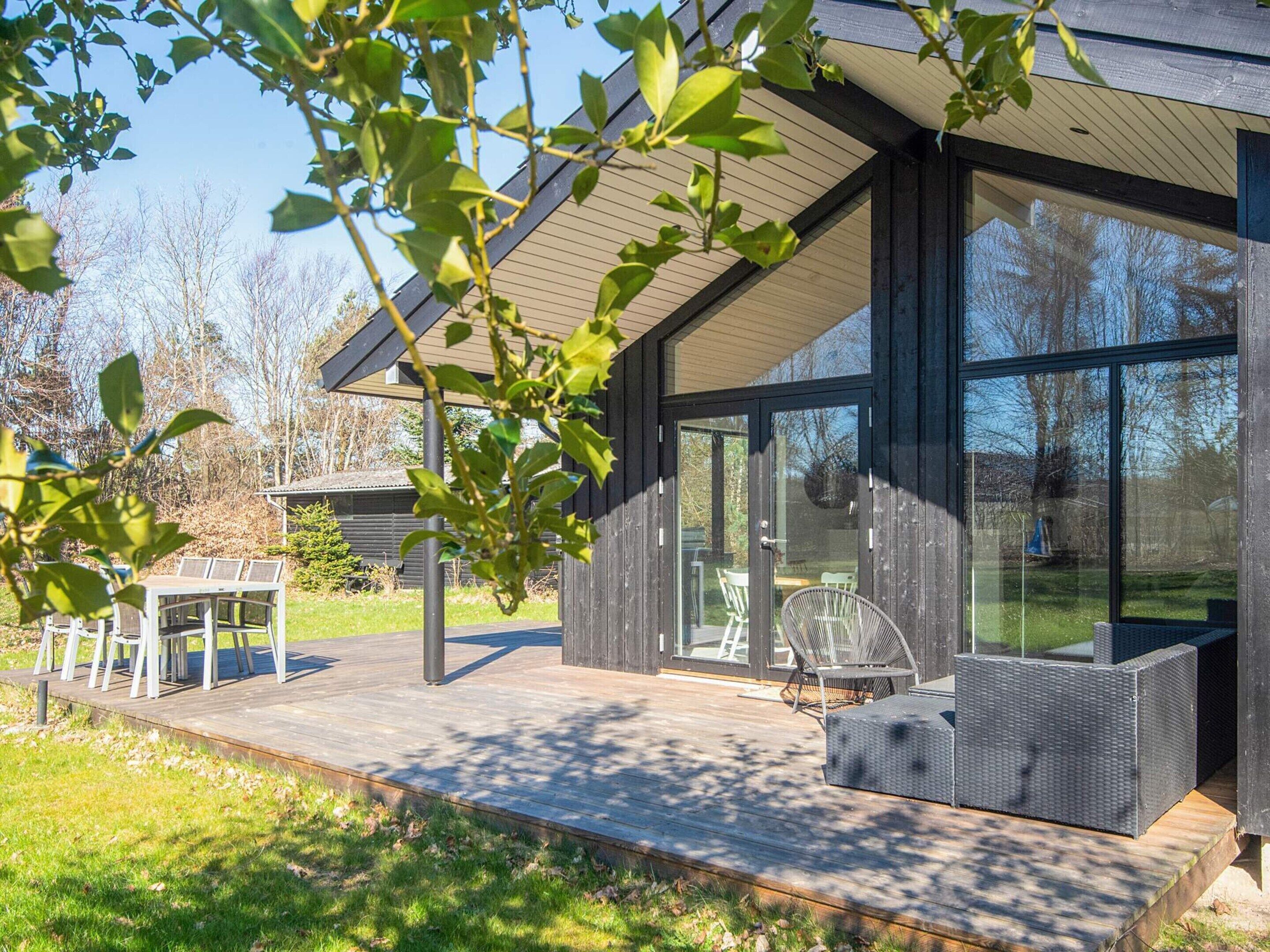 Ein modernes Haus mit einem großen Panoramafenster, einer Holzterrasse und Gartenmöbeln.