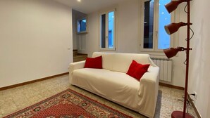 A white sofa with red cushions, a patterned rug, and a floor lamp in a room with white walls and a window. - Figher 795 ( near the Rialto Bridge ) (Venezia)