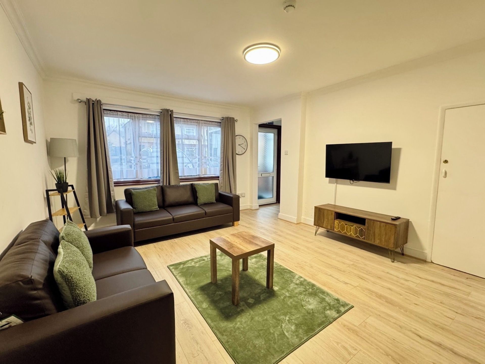 Una sala de estar moderna con sofá, mesa de centro, televisor y ventana con cortinas.