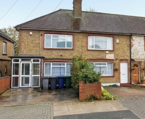 A two-story brick house with a front garden, a garage, and a small attached structure with a glass door. - Modern 3BDR Family Home Near Welsh Harp Hendon (Greater London)