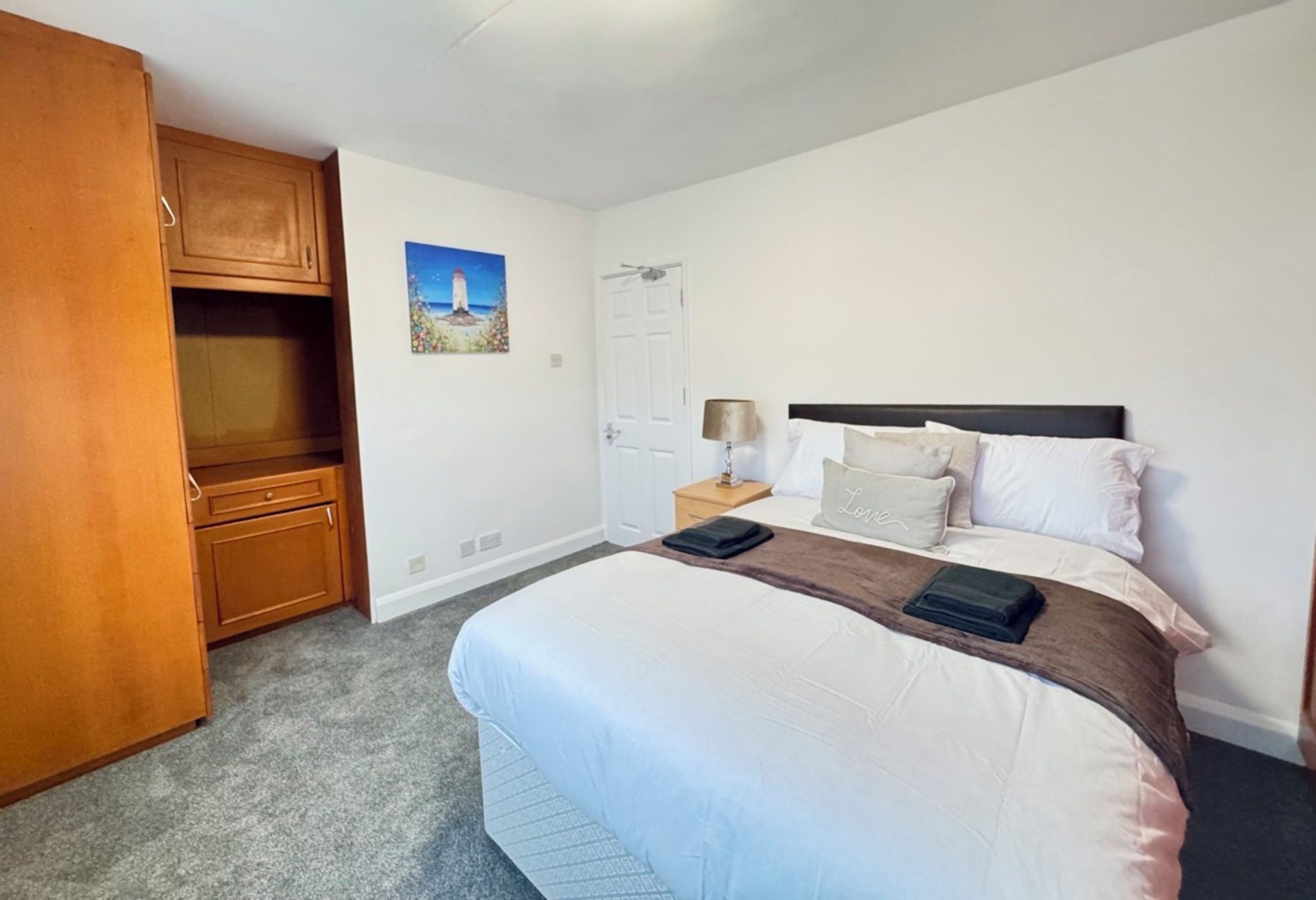 A bedroom with a bed, a nightstand, a lamp, a wardrobe, and a painting on the wall.