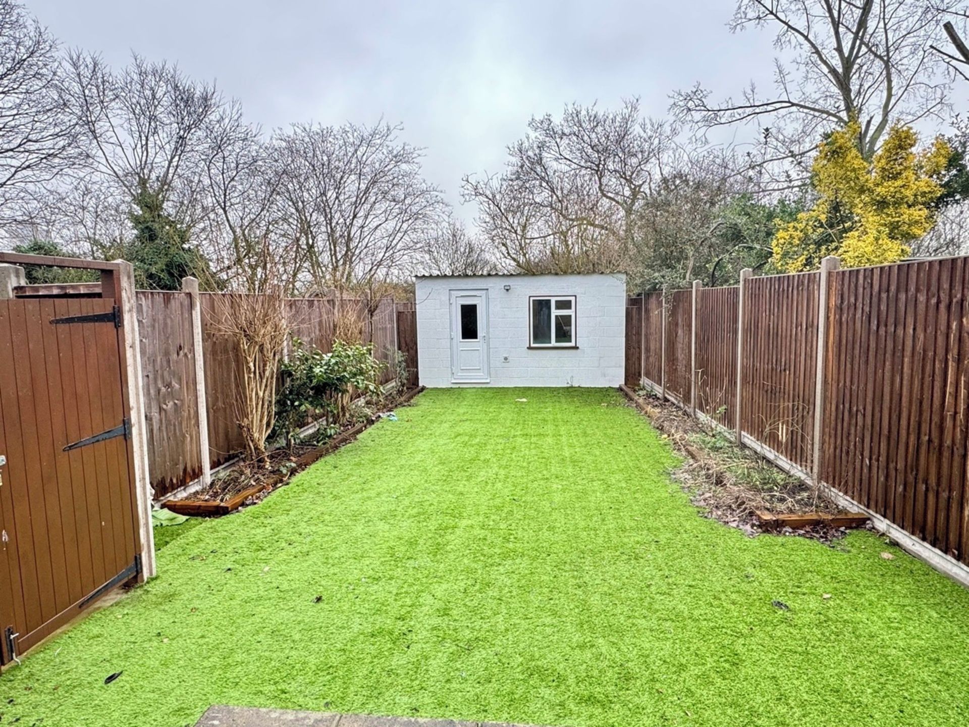 Un patio trasero cercado con un cobertizo pequeño, un portón de madera y un césped.