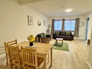 A modern living room with a dining area, featuring a sofa, a coffee table, and a dining table with chairs. - Modern 3BDR Family Home Near Welsh Harp Hendon (Greater London)