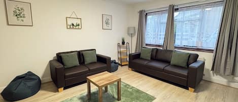 Een woonkamer met twee banken, een salontafel, een relaxstoel en een groen vloerkleed.