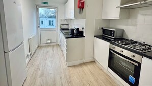 A modern kitchen with white cabinets, a gas stove, a microwave, and a refrigerator. - Modern 3BDR Family Home Near Welsh Harp Hendon (Greater London)