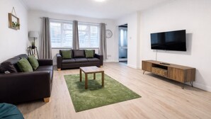 A modern living room with a sofa, a coffee table, a TV, and a wooden cabinet. - Modern 3BDR Family Home Near Welsh Harp Hendon (Greater London)