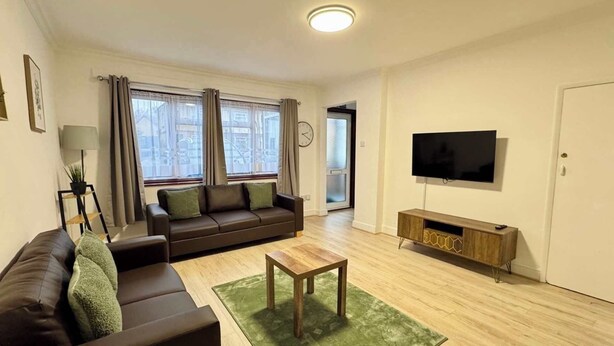 A living room with a sofa, a coffee table, a TV, and a door. - Modern 3BDR Family Home Near Welsh Harp Hendon (Greater London)