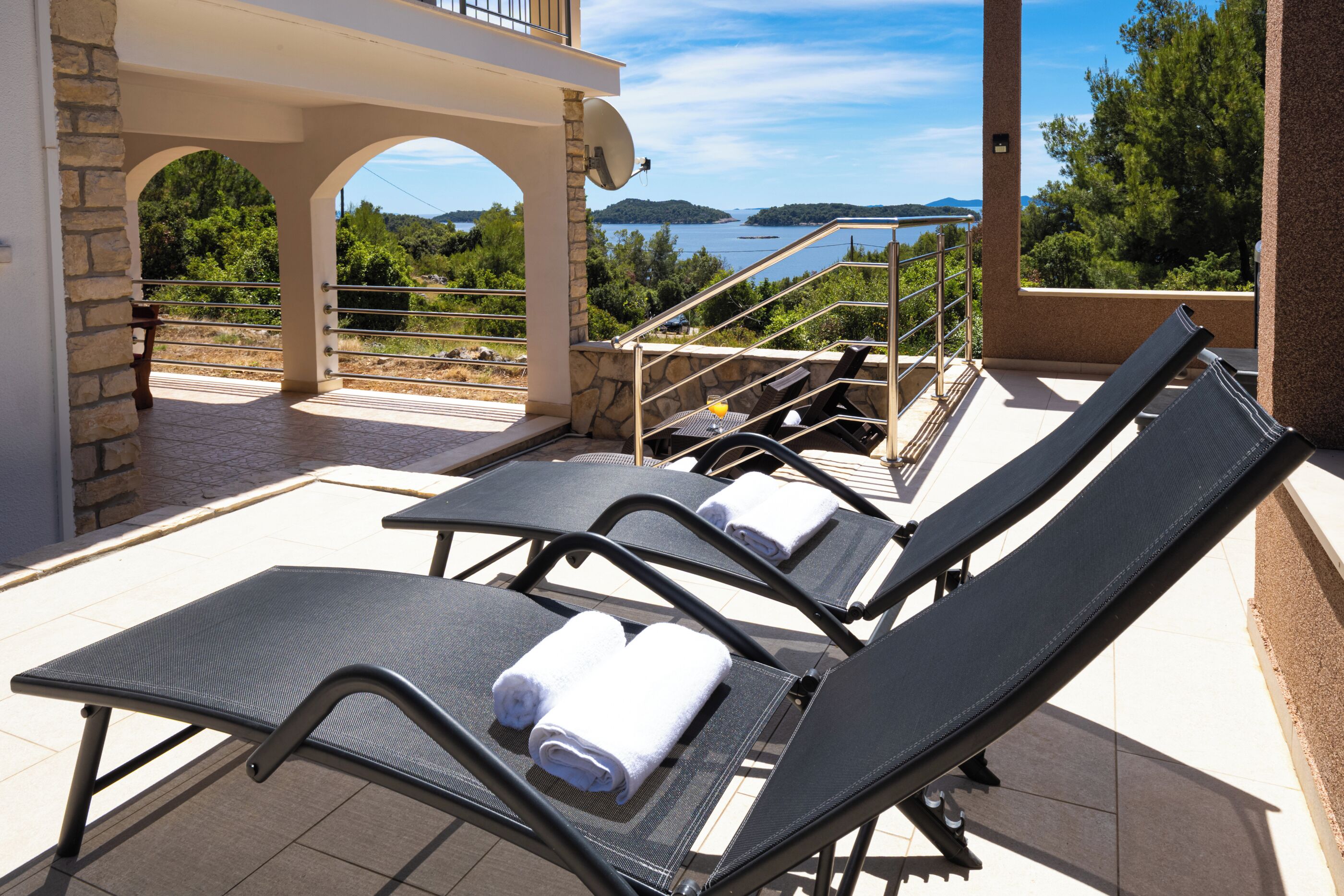 A terrace with sun loungers, a stone wall, and a view of a lake.