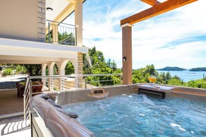 Ein Whirlpool mit einem Glas Orangensaft auf einem Balkon mit Blick auf ein Gewässer.