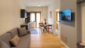 Ein modernes Wohnzimmer mit einer Couch, einem Essbereich mit Tisch und Stühlen, einer Küche mit Schränken und einem flachbildfernseher an der Wand.