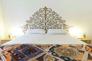 Una cama con un cabecero decorativo, ropa de cama blanca y una manta estampada.