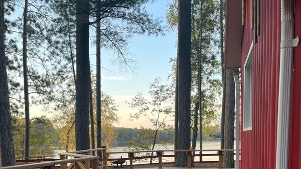A wooden deck with picnic tables and a red building in the background. - Beautiful one acre 3 bedroom Private boat and snowmobile launch (Saint Germain)