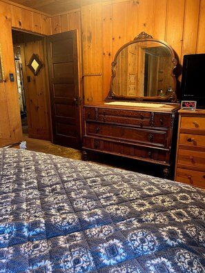 A bedroom with a wooden wardrobe, a mirror, and a bed with a patterned duvet.