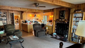 A cozy living room with a fireplace, a bookshelf, and a dining area with wooden cabinets. - Beautiful one acre 3 bedroom Private boat and snowmobile launch (Saint Germain)