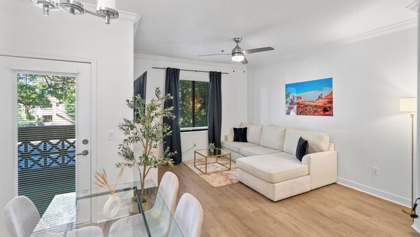 A modern living room with a glass dining table, a beige sofa, a ceiling fan, and a view of the outdoors through a door. - San Portella 2019 (Tempe)