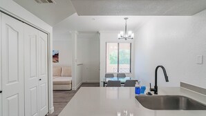 A kitchen with a central island, a built-in dishwasher, a black faucet, and a dining area with a table and chairs. - San Portella 2019 (Tempe)