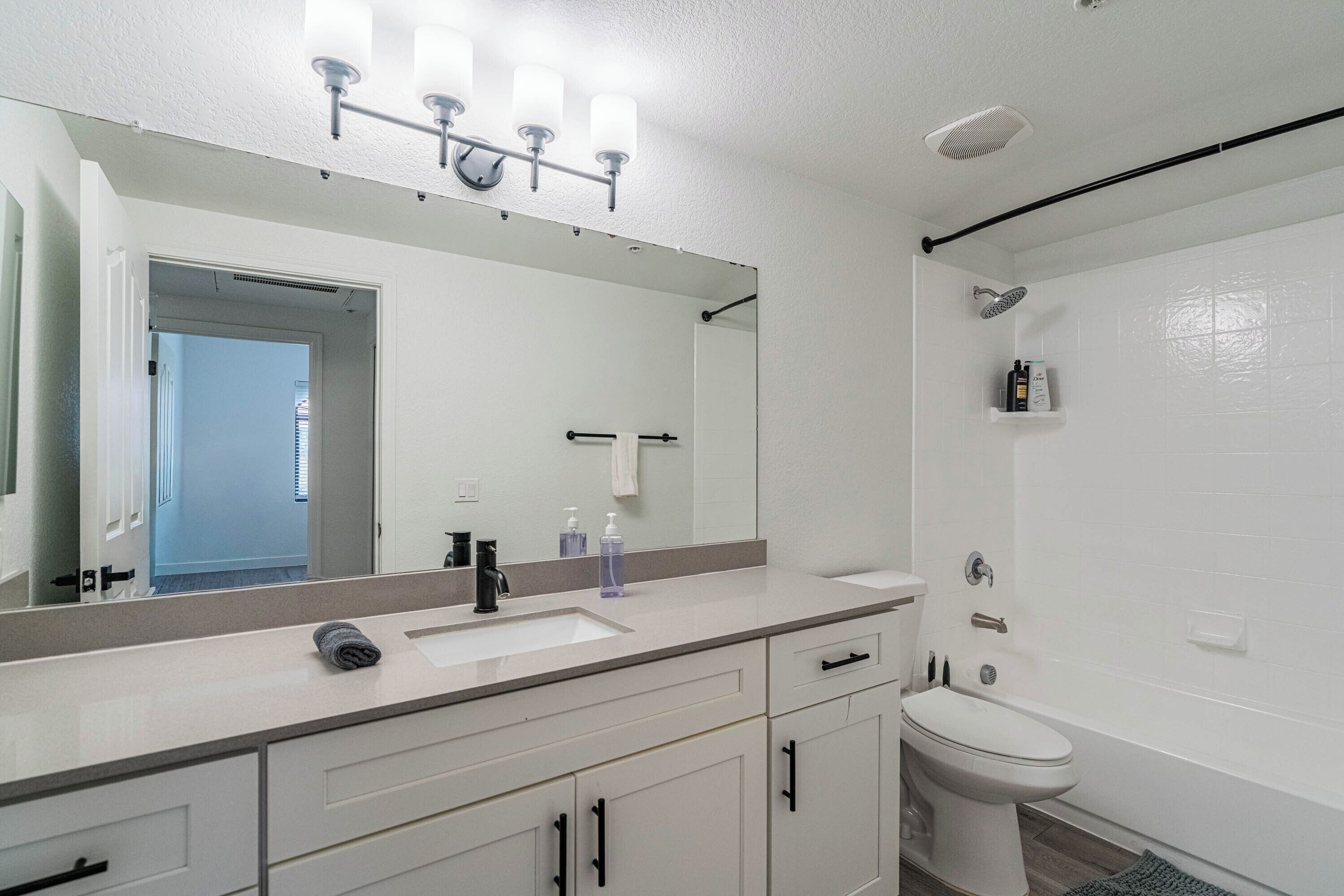 A modern bathroom with a large mirror, a sink, a toilet, and a shower area.