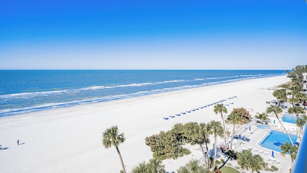A beach resort with a pool, palm trees, and a clear blue sky. - SC1-802 | Gulf-Front 3BR Condo • Direct Balcony Views (Indian Shores)