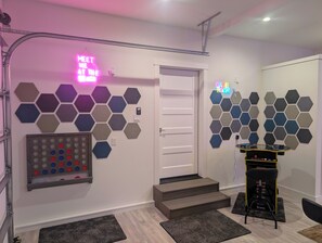 A room with a neon sign, hexagonal wall decor, a game table, and a door.