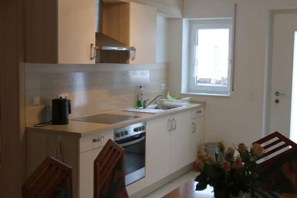 A compact kitchen with a built-in oven, a window, and a dining area with a table and chairs.