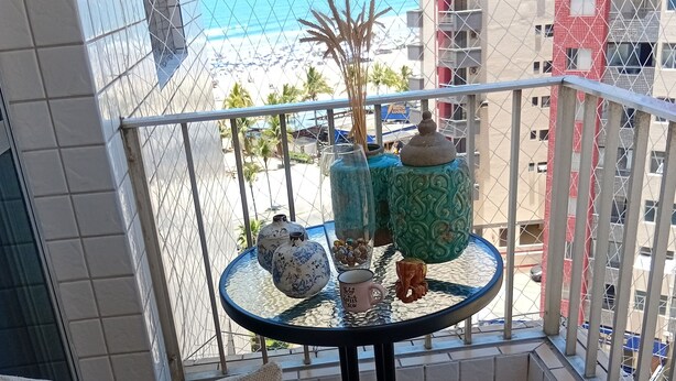 En balkon med et bord, to stole, pyntetinge og udsigt til strand og hav.