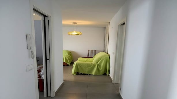 Un pasillo estrecho que conduce a una habitación con una cama cubierta de sábanas verdes.