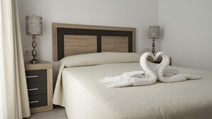 Habitación de hotel con cama, dos lámparas de noche, cabecero de madera y una decoración de toallas con forma de cisne.
