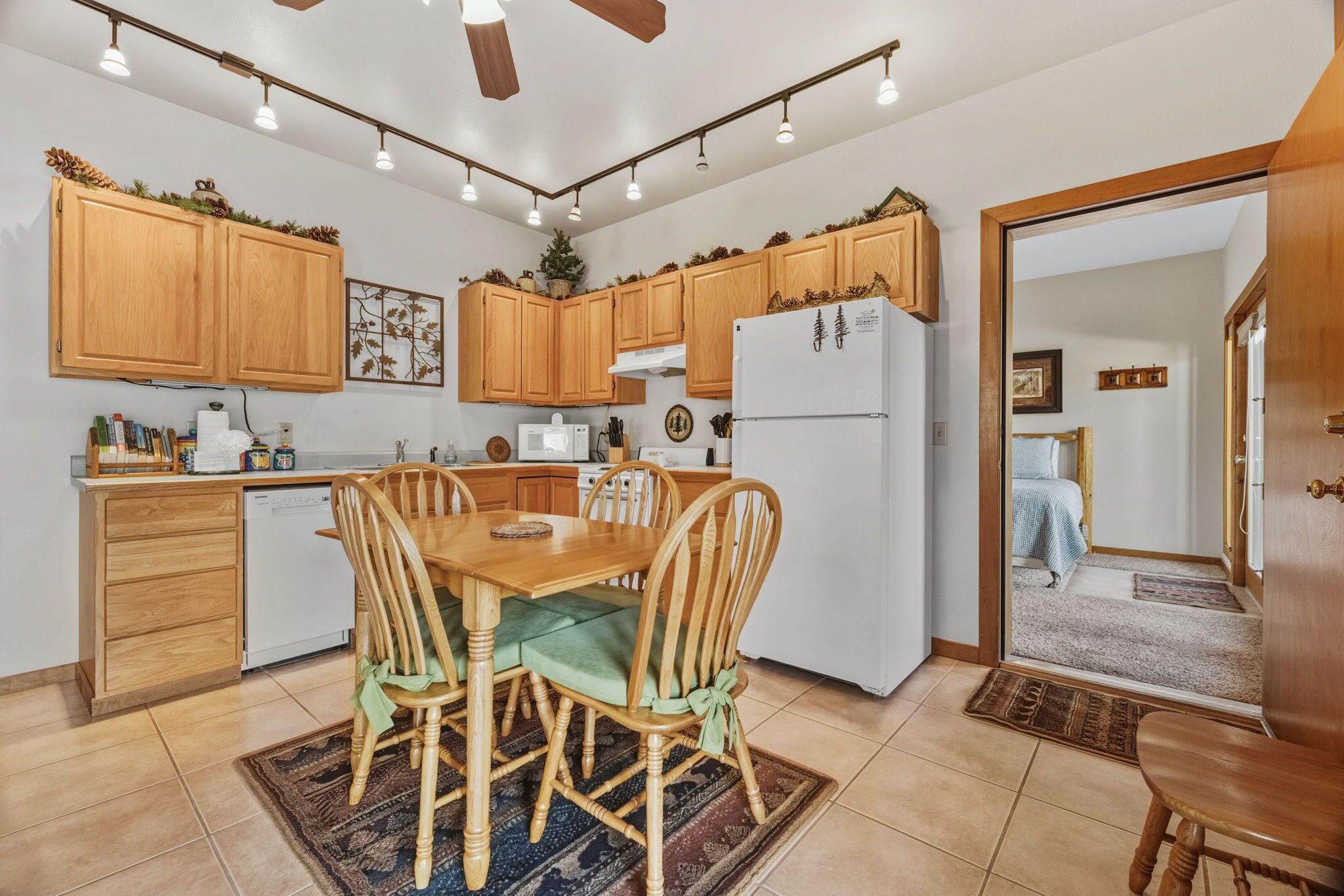 A kitchen with wooden cabinets, a dining table with chairs, a refrigerator, and a ceiling fan.