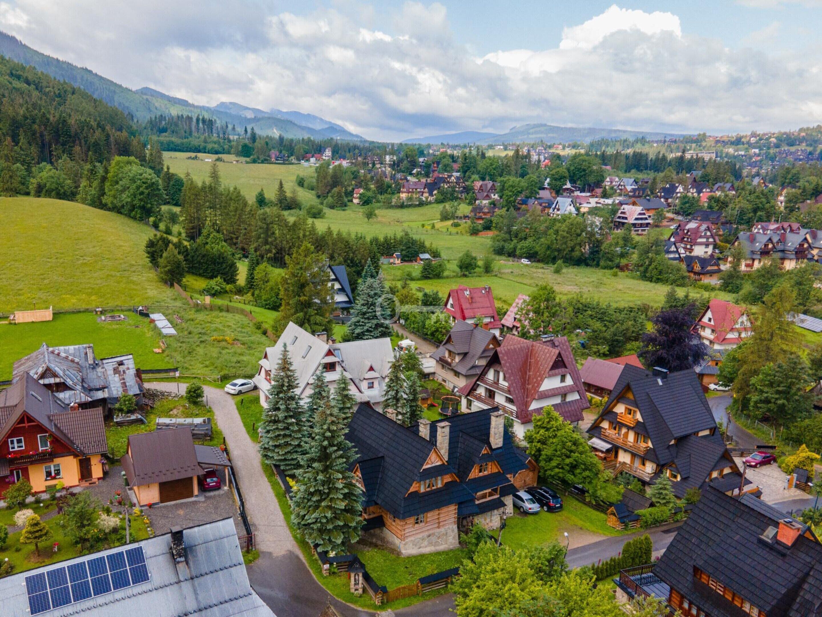 Un village rural avec des maisons traditionnelles, un grand champ verdoyant et des montagnes en arrière-plan.