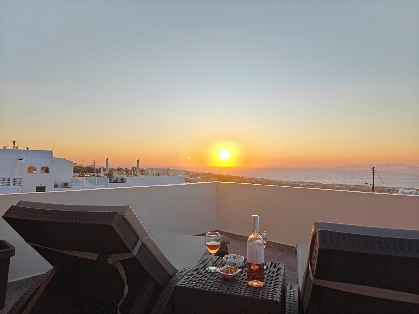 A sunset view from a balcony with a table set for two, including a bottle and glasses.